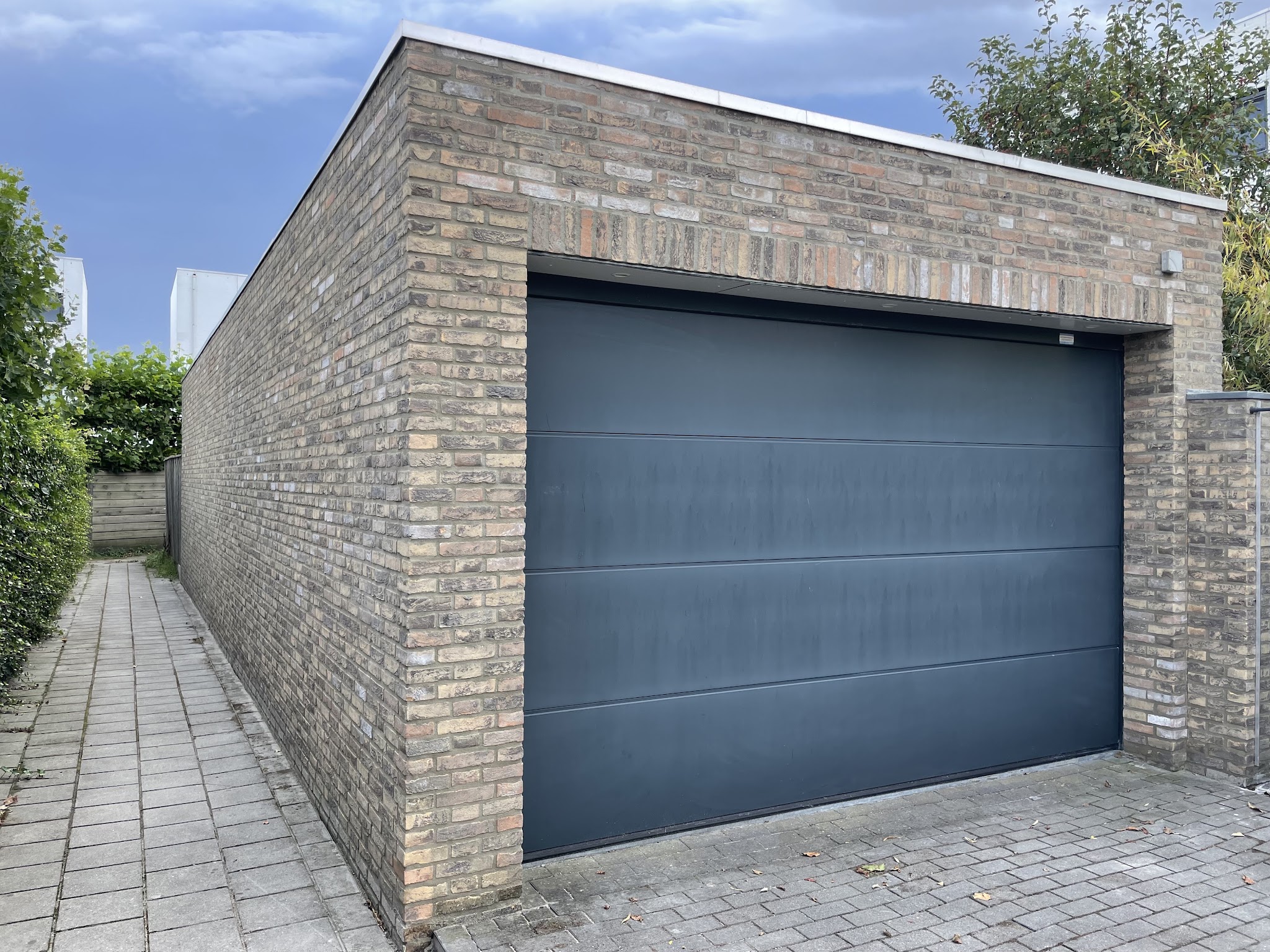 Een garage van gele en grijze baksteen met strak voegwerk en een antracieten garagedeur